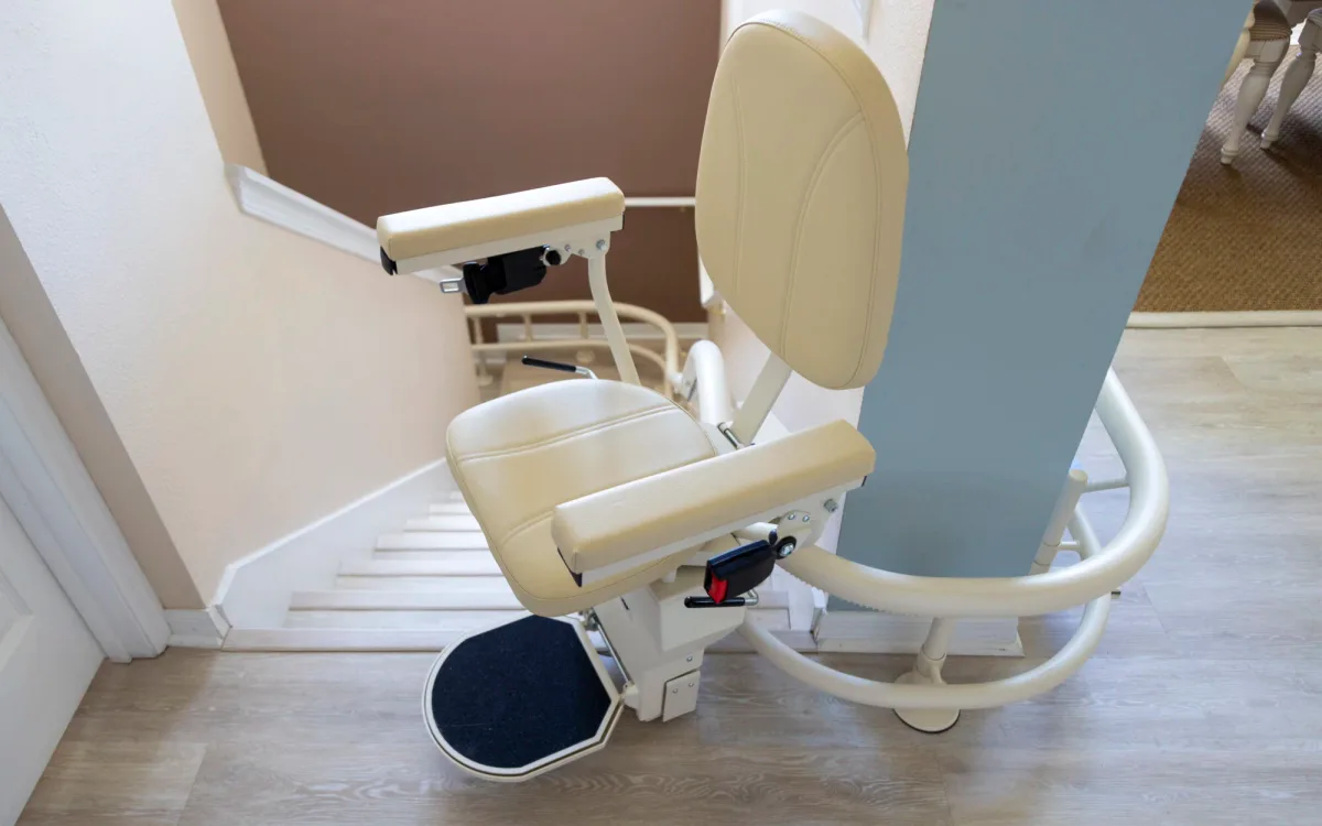 Curved stairlift parked at the foot of the stairs, its rail curving around onto the hallway floor