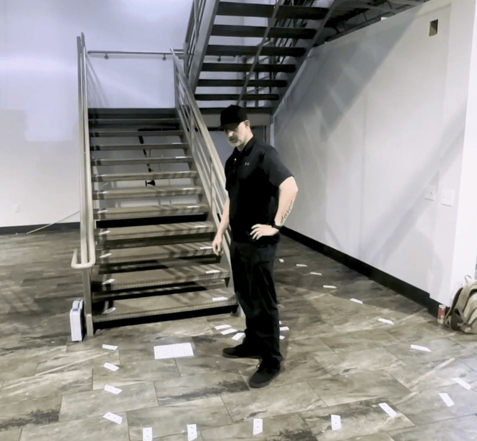 Technician surveying a staircase for a curved stairlift, with photogrammetry markers laid out on the floor and treads