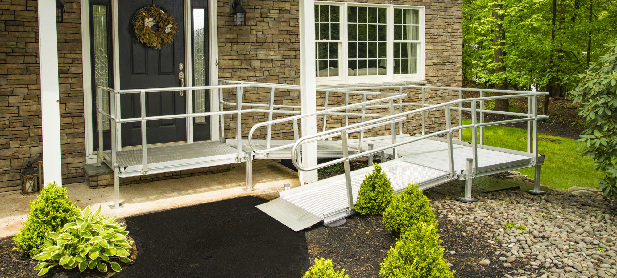 Modular aluminum ramp with platform and handrails installed at a stone-front home entrance