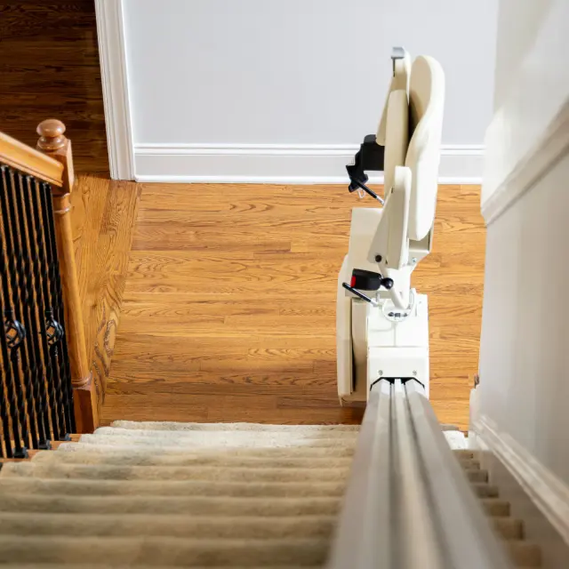 Straight stairlift with the seat folded up, viewed from the top of a carpeted staircase